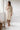 Woman in an oatmeal Turkish cotton muslin robe holding a coffee in a bright bathroom