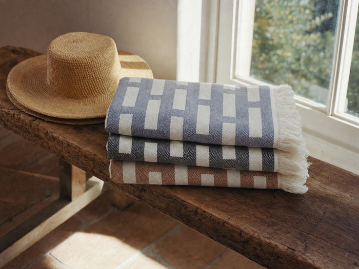 Jacquard Turkish cotton beach towels in blue, black and cinnamon folded on a wooden bench